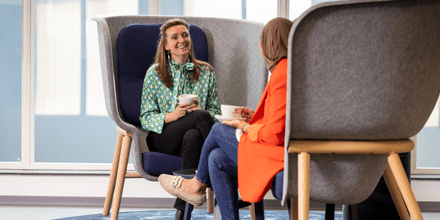 Twee collega's drinken koffie en zitten in hoge grijze stoelen