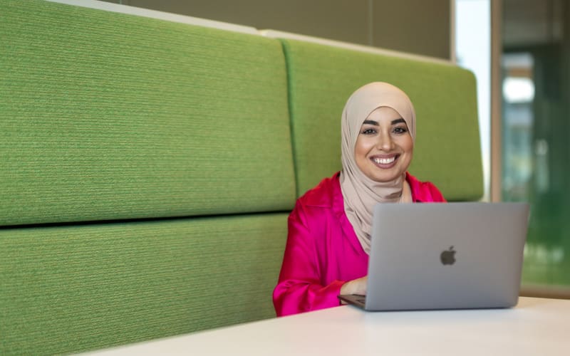 vrouw zit lachend te werken achter haar laptop