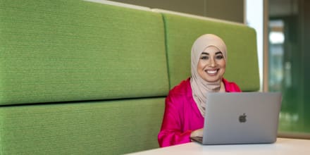 vrouw zit lachend te werken achter haar laptop